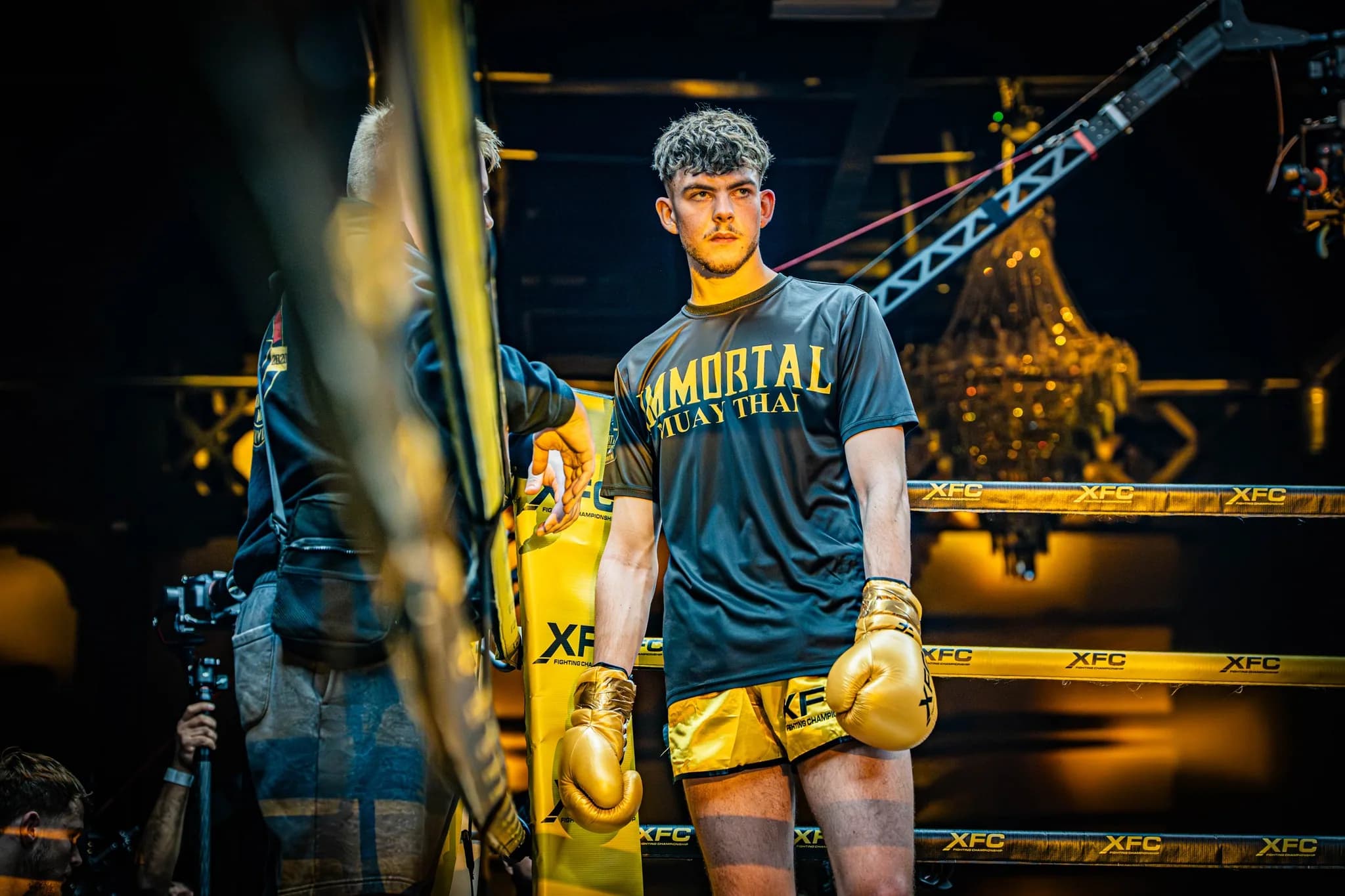 Gloved XFC fighter standing in the corner under low event lighting.