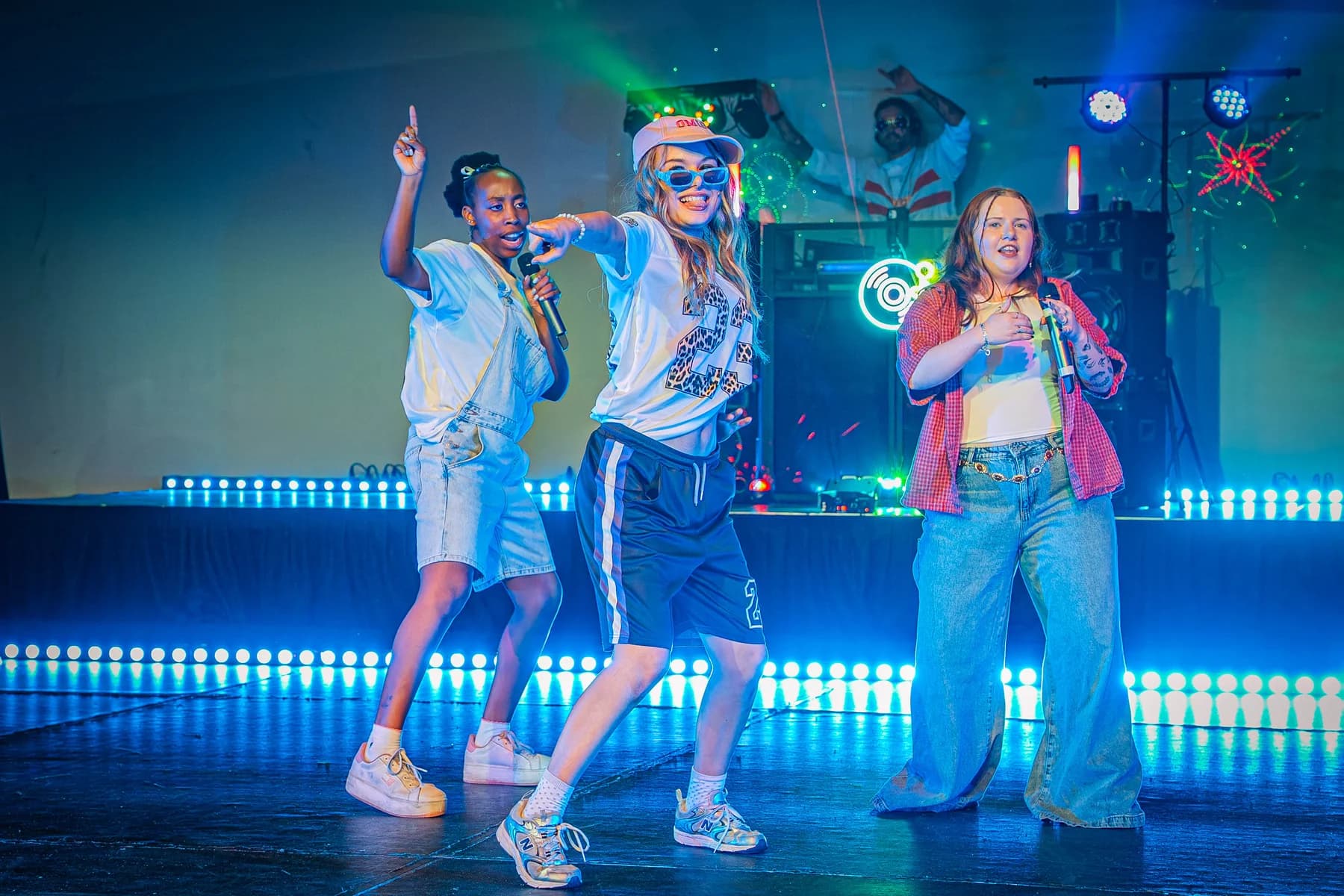 Three performers singing under blue stage lighting during a 90s musical show.