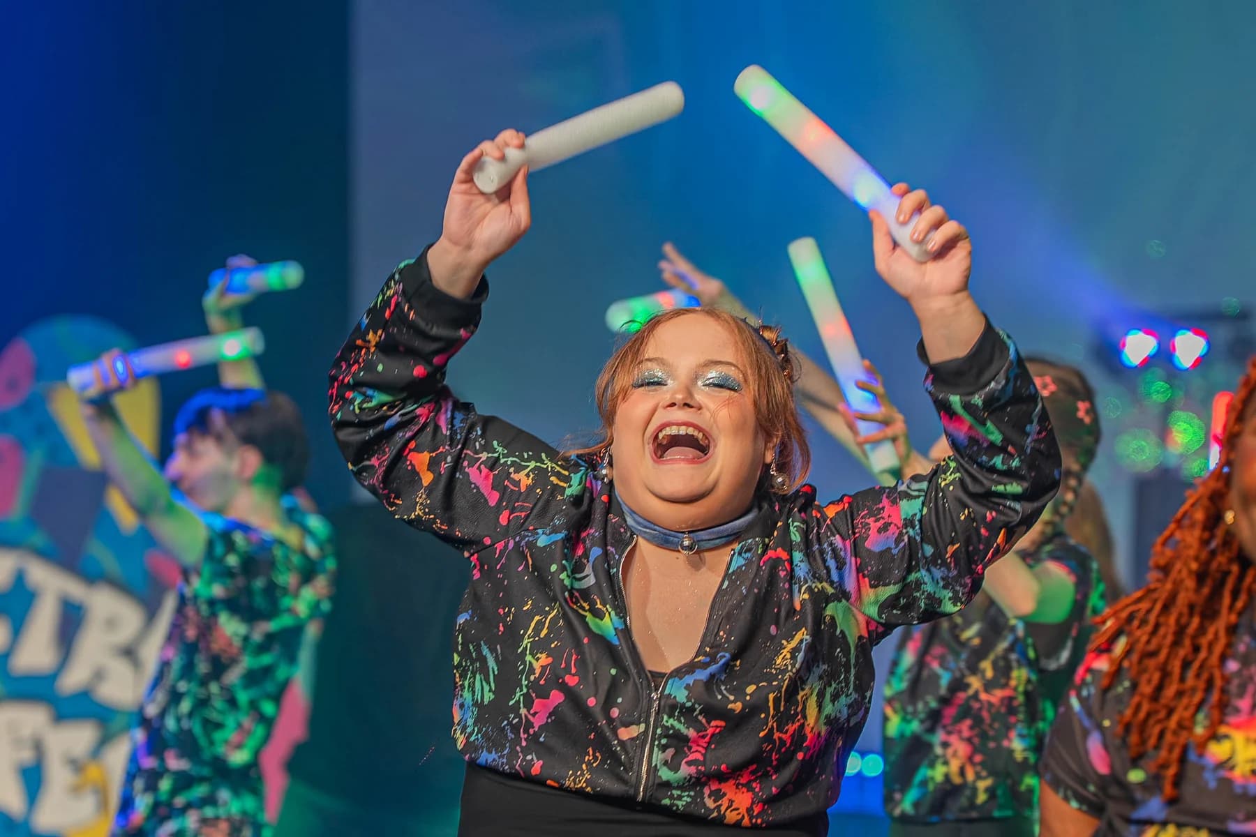 Performer smiling with glow sticks during a 90s musical show.