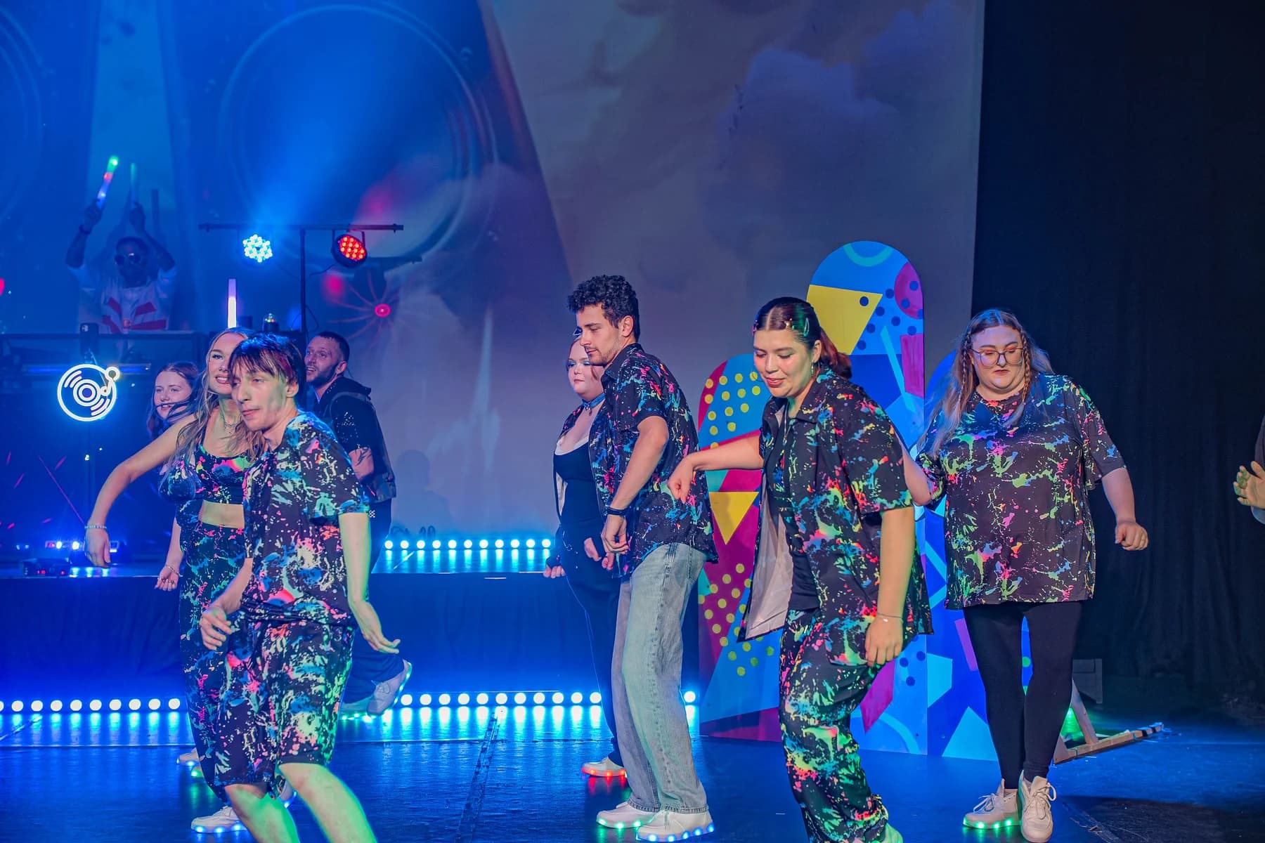 Ensemble cast performing under low-light stage lighting.