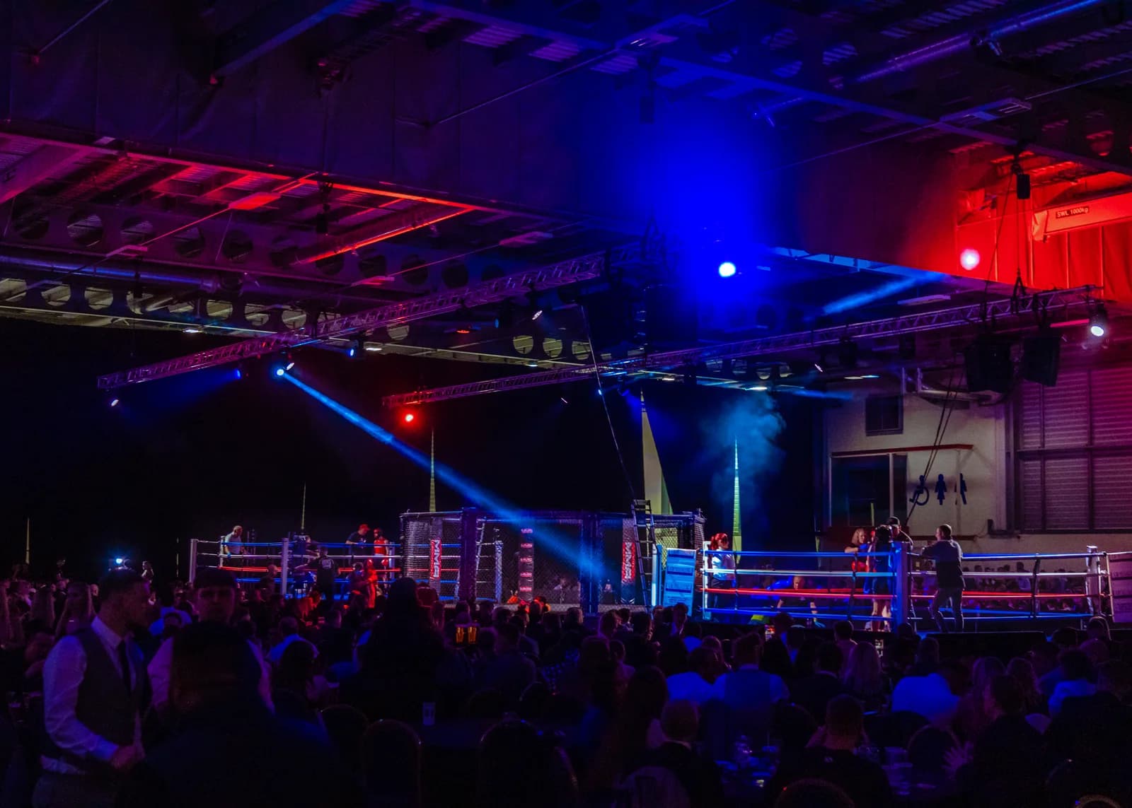 Wide view of a combat sports venue with ring lighting and production beams before the action.