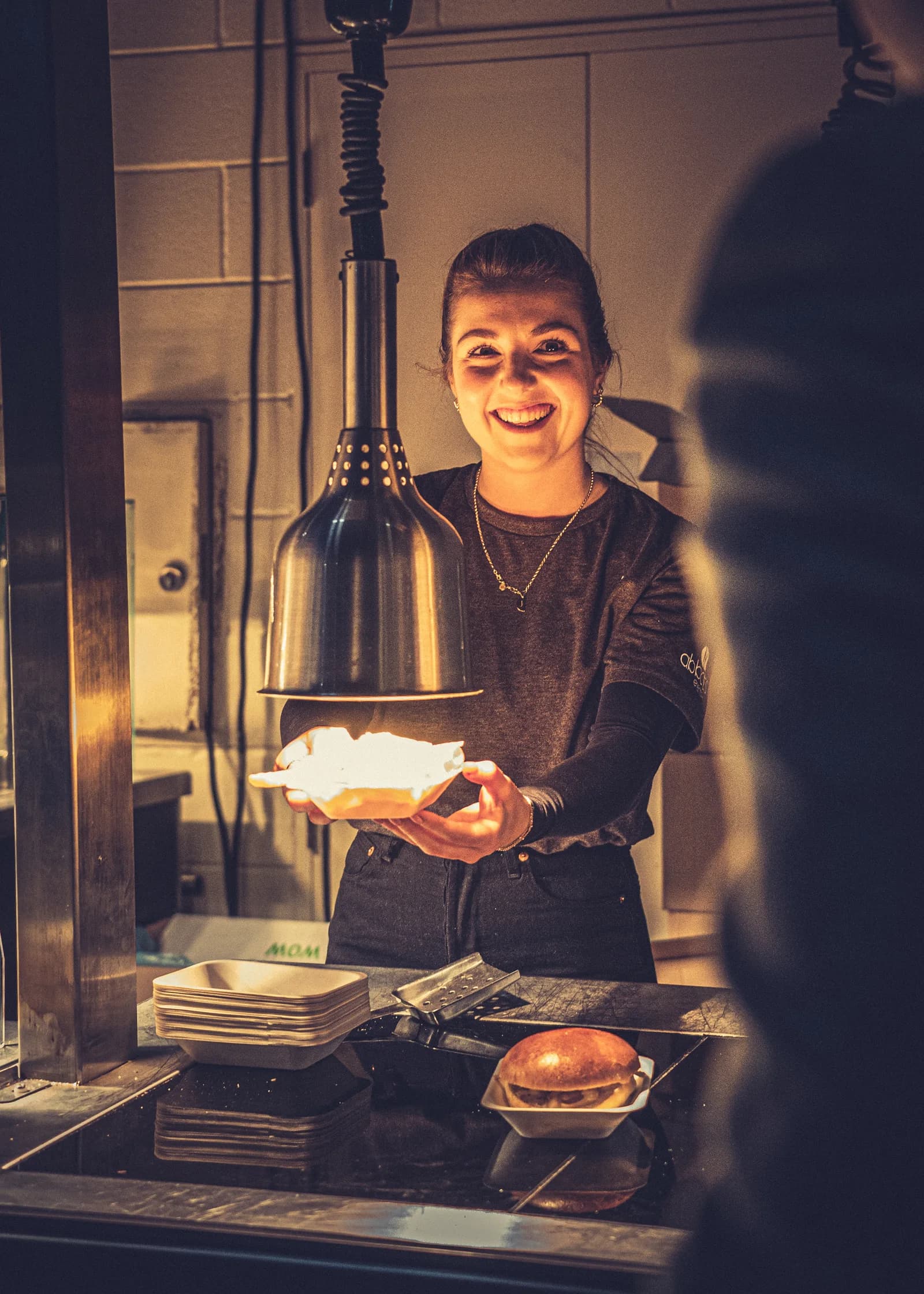 Smiling event staff member serving food under warm hospitality lighting.