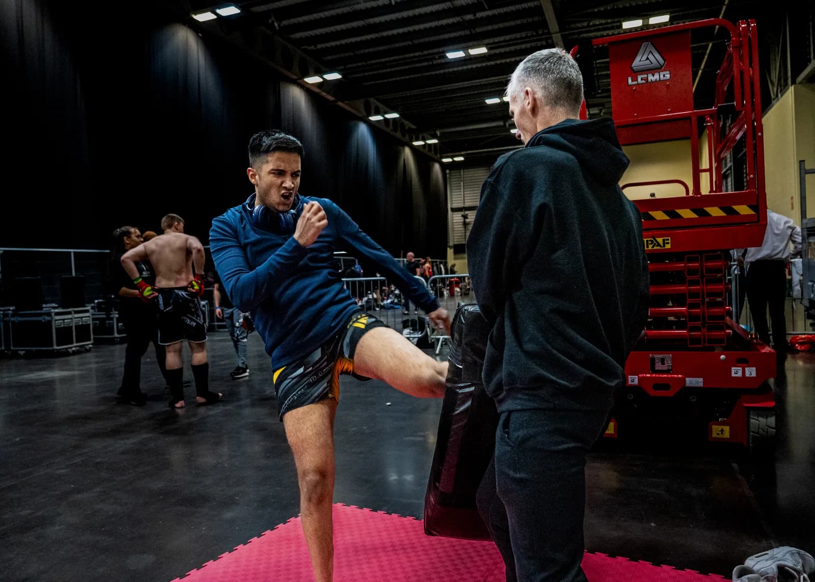 Fighter warming up with a kick while a coach watches before a combat sports bout.