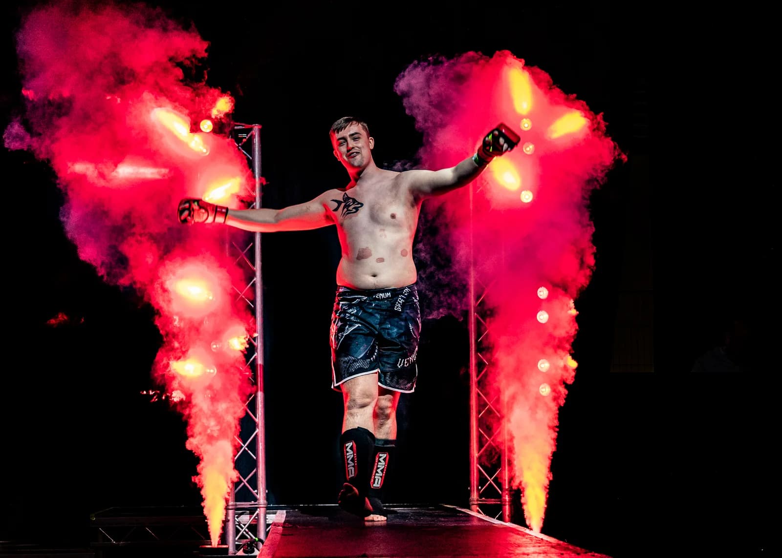 Fighter celebrating between red pyrotechnics on a live walkout stage.