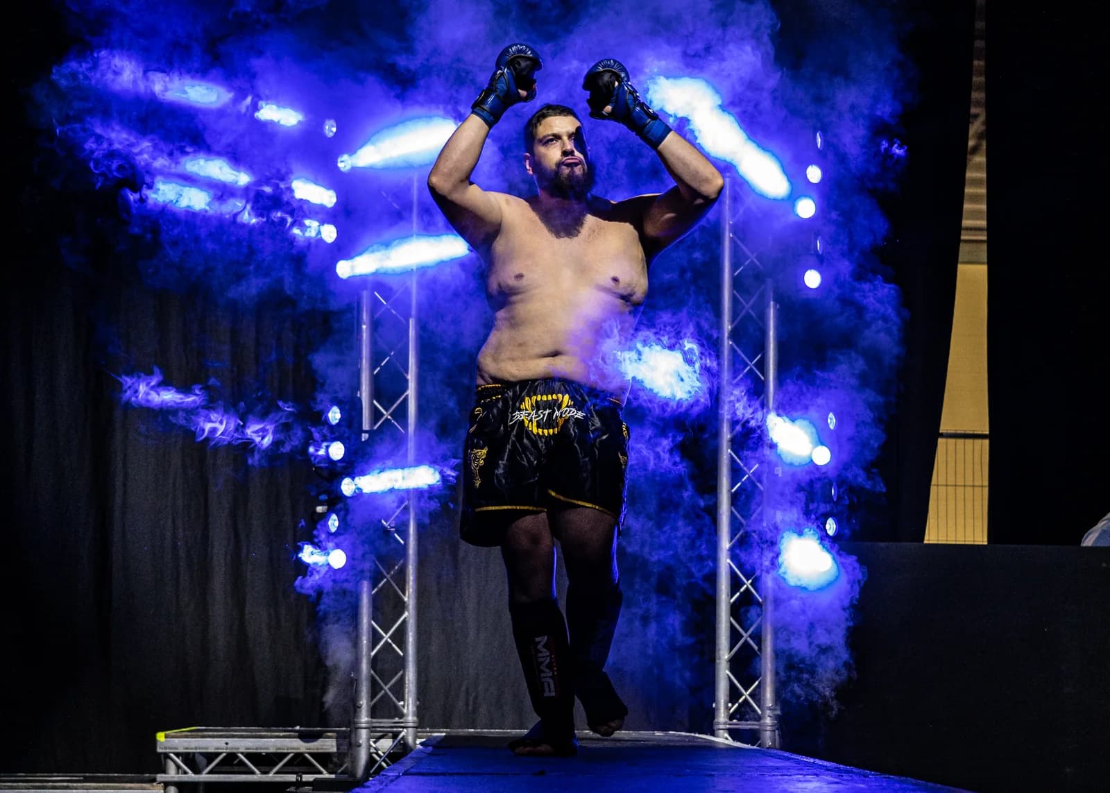 Fighter raising both arms during a blue-lit walkout entrance with smoke and stage lighting.
