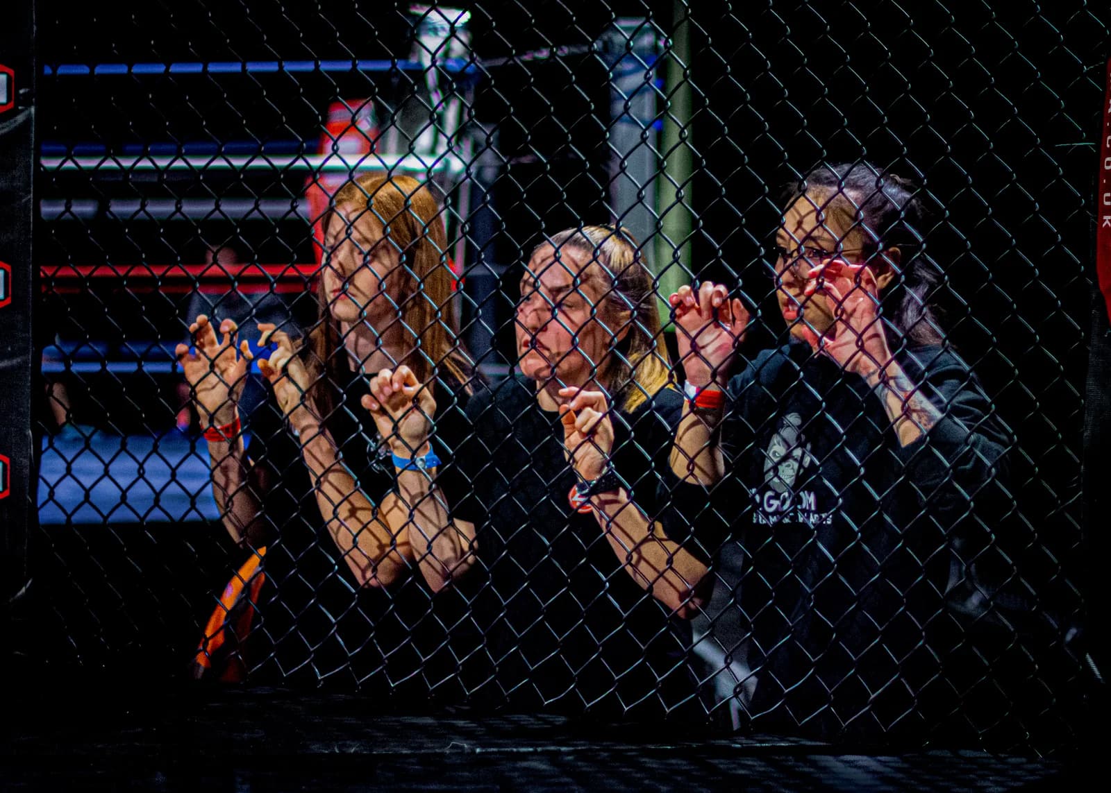 Cage-side team moment with coaches and fighter gathered behind the fence during an MMA event.